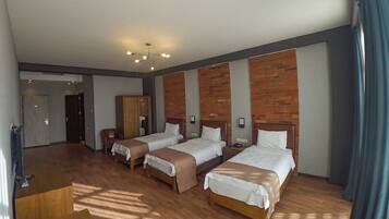 Een hotelkamer met vier eenpersoonsbedden, een houten bureau, een kledingkast en een accentmuur van baksteen.