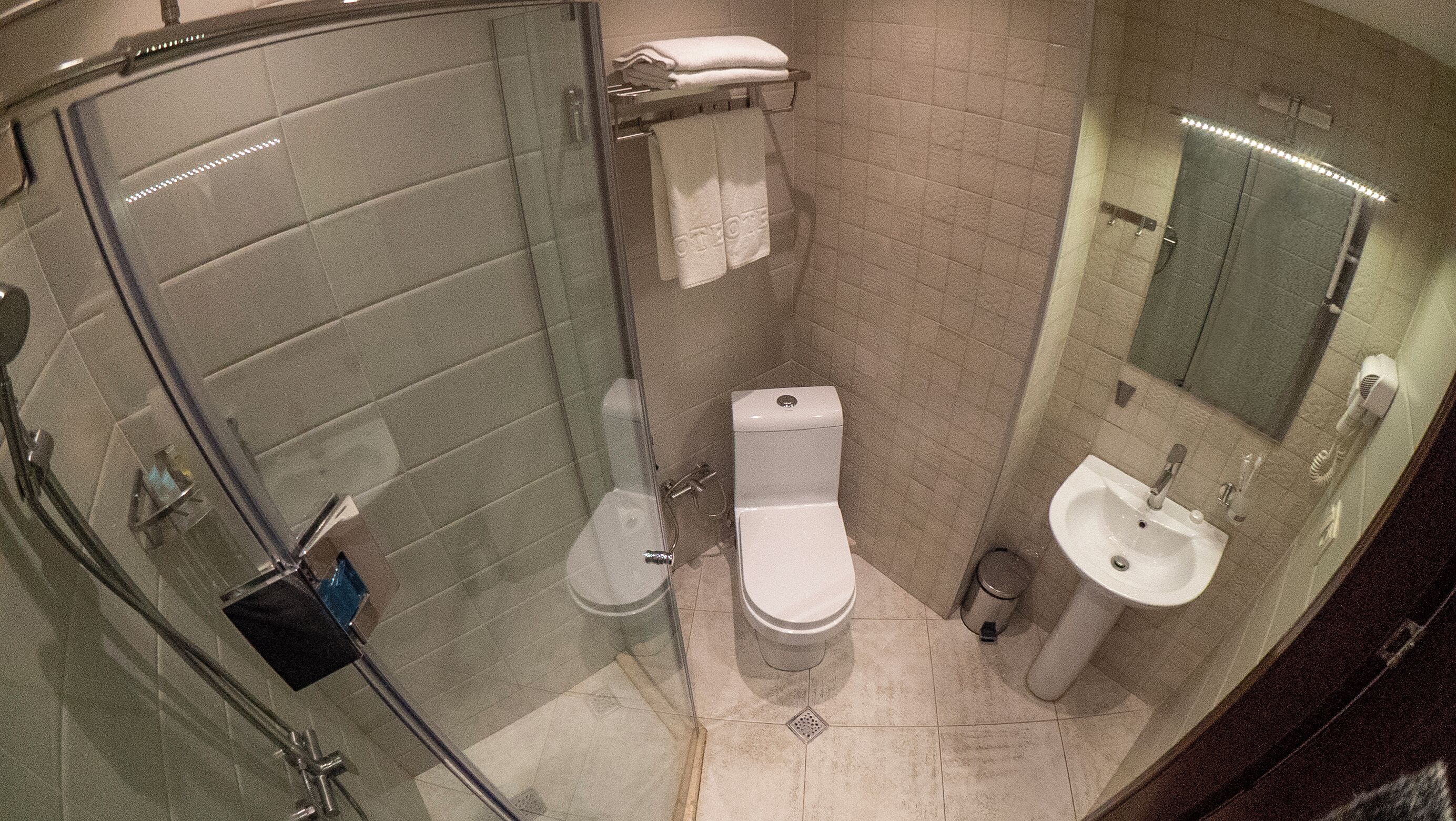Uma casa de banho compacta com cabine de duche em vidro, sanita, lavatório e suporte para toalhas.