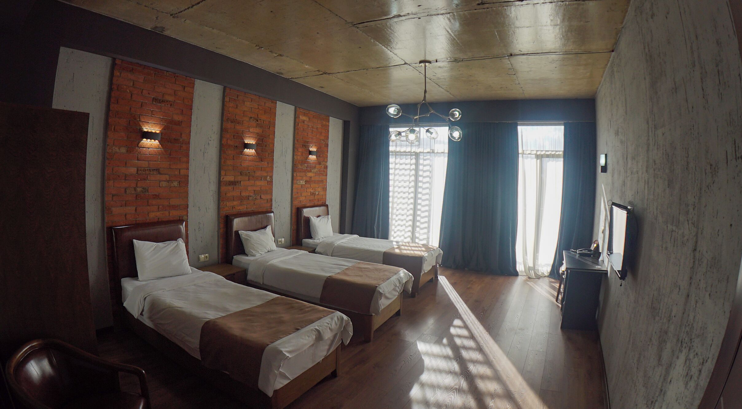Een hotelkamer met drie bedden, bakstenen muren en een houten plafond.