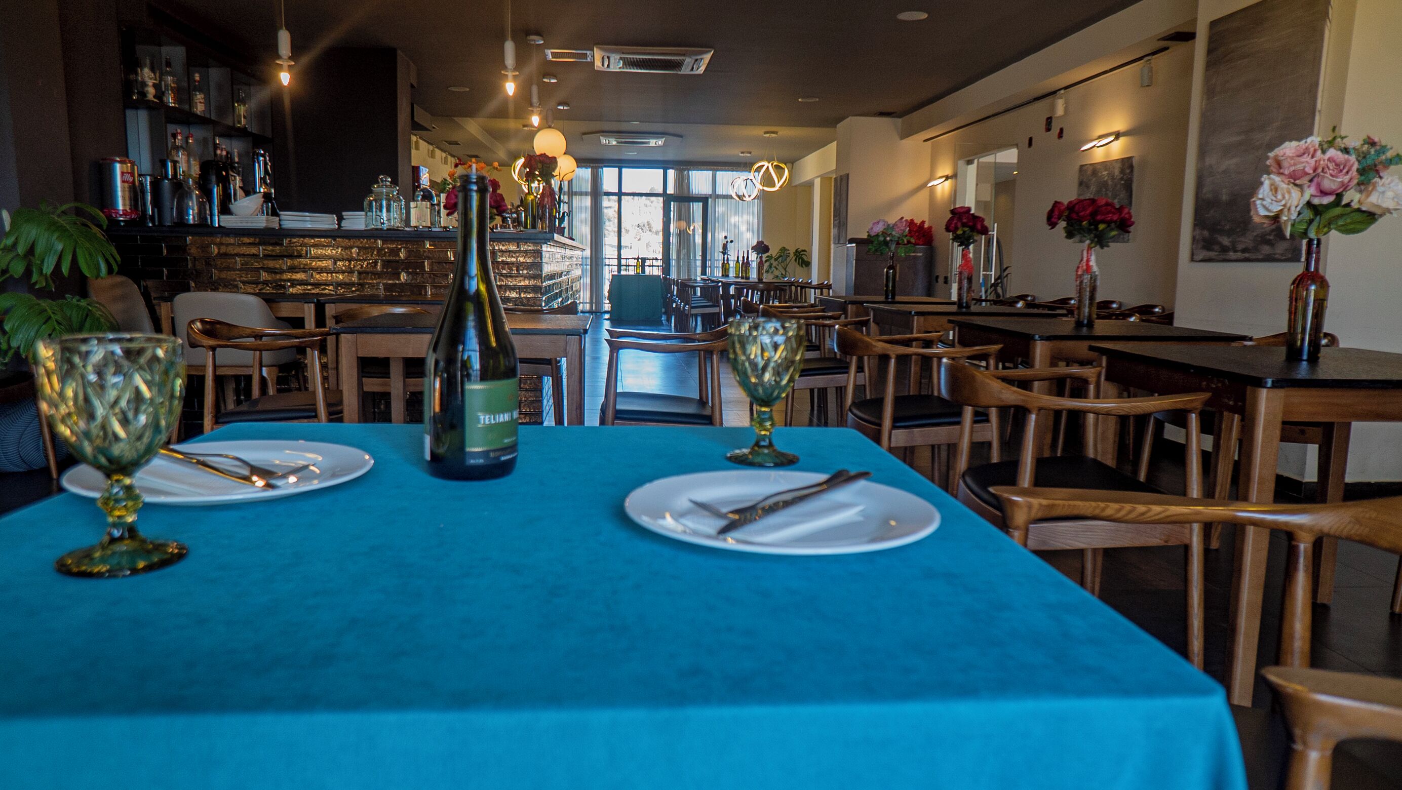 Un restaurant avec des tables dressées pour le service, un bar en arrière-plan et diverses bouteilles et verres disposés sur le comptoir du bar.
