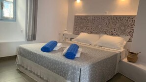 A neatly made bed with a patterned bedspread and two rolled towels, a decorative headboard, a bedside lamp, and a small woven basket on the nightstand. - Au Cœur de Parikia , Appartement Cosy Avec Balcon (Parikiá)