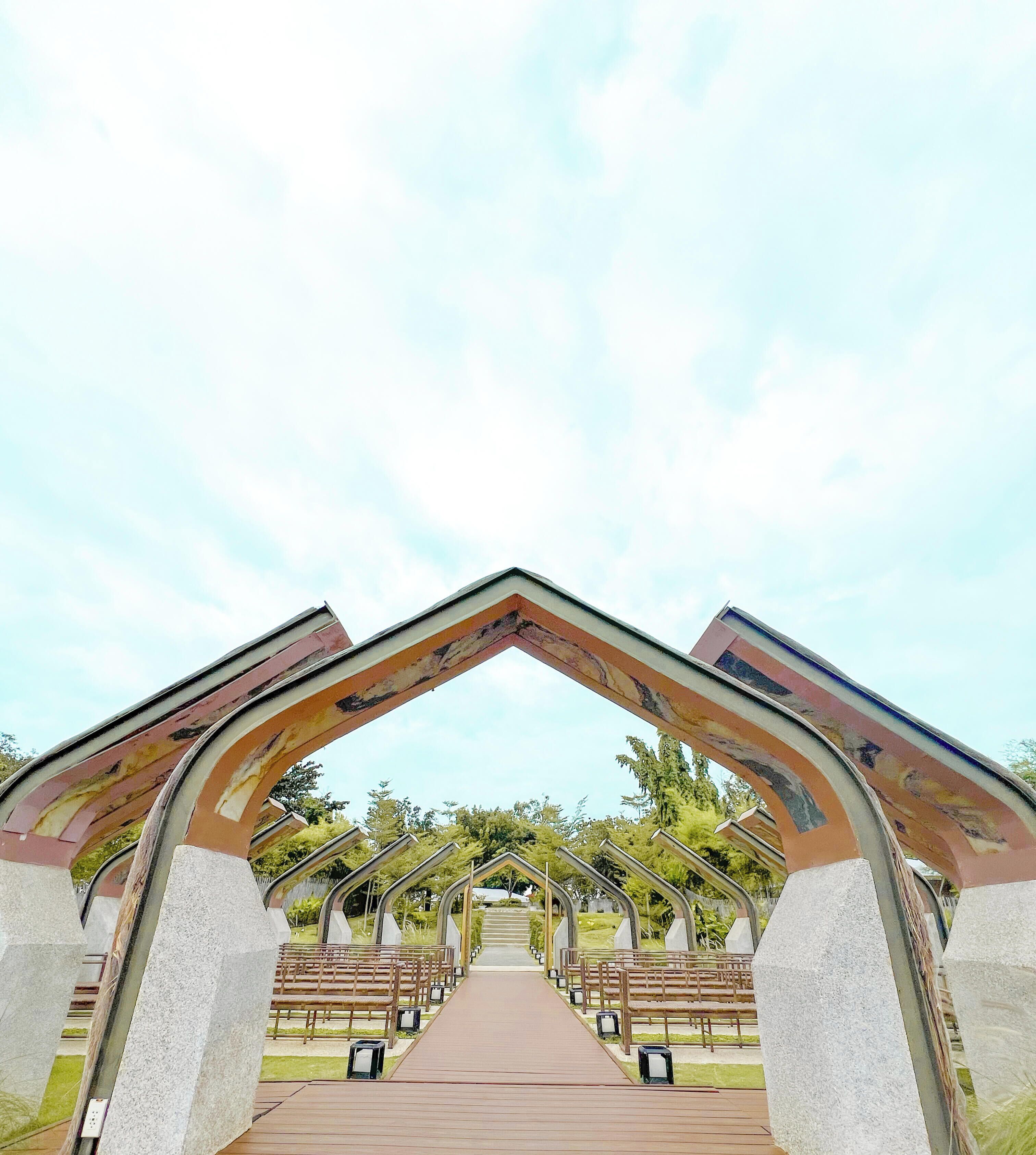A pathway leading through a structure with a series of arches, benches, and a clear sky.