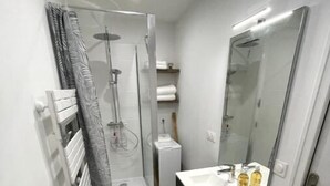 Et lille badeværelse med toilet, brusekabine med glasdør, vask med spejl og håndklædestang.