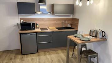 Een compacte keuken met een vaatwasser, magnetron, spoelbak en een klein eethoekje met krukken.