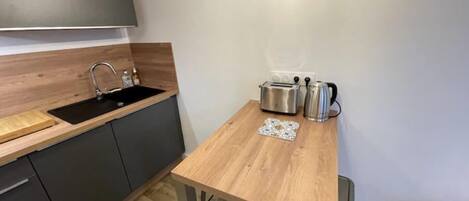 A compact kitchen with a wooden countertop, a sink, a toaster, and a kettle.