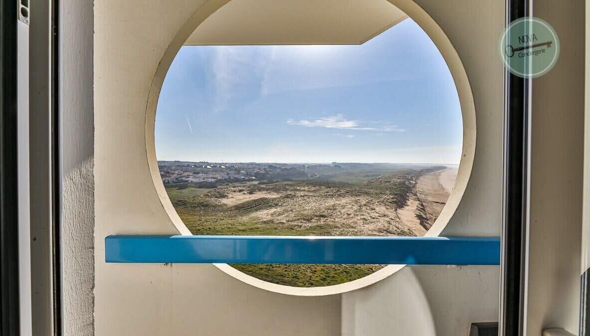 Une fenêtre circulaire donnant sur un paysage désertique, une étagère bleue et un logo sur le mur.