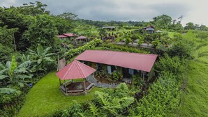 Un bungalow avec un toit rouge, entouré d’une végétation luxuriante et d’un petit jardin.
