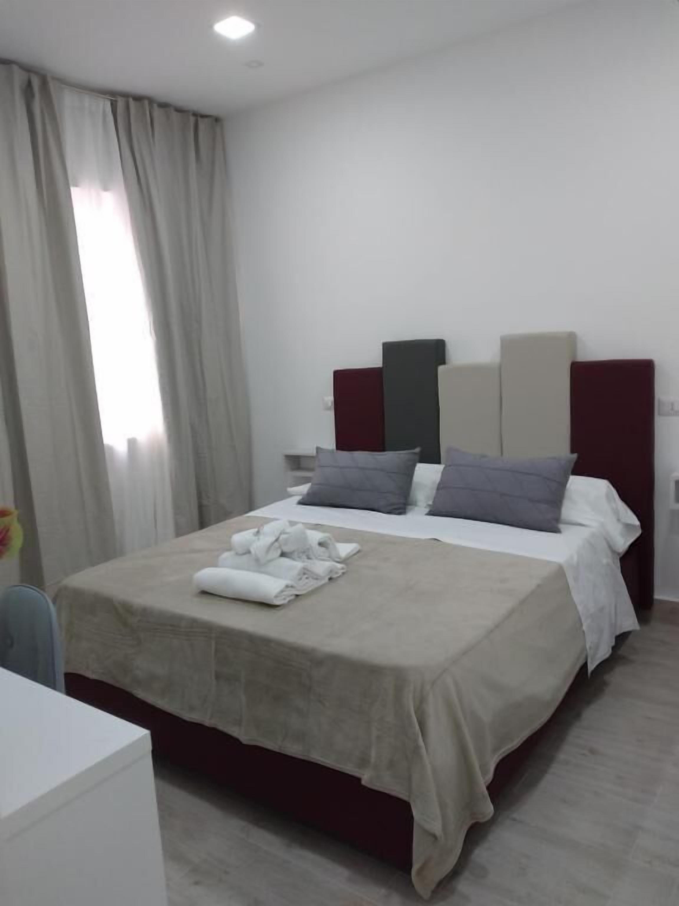 Quarto de hotel com cama, escrivaninha e janela com cortinas.