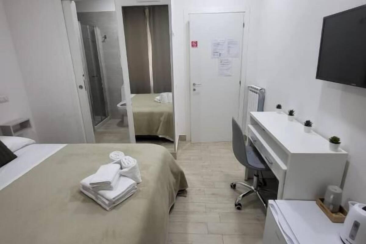 A hotel room with a bed, a desk, a chair, a TV, and a small kitchenette.