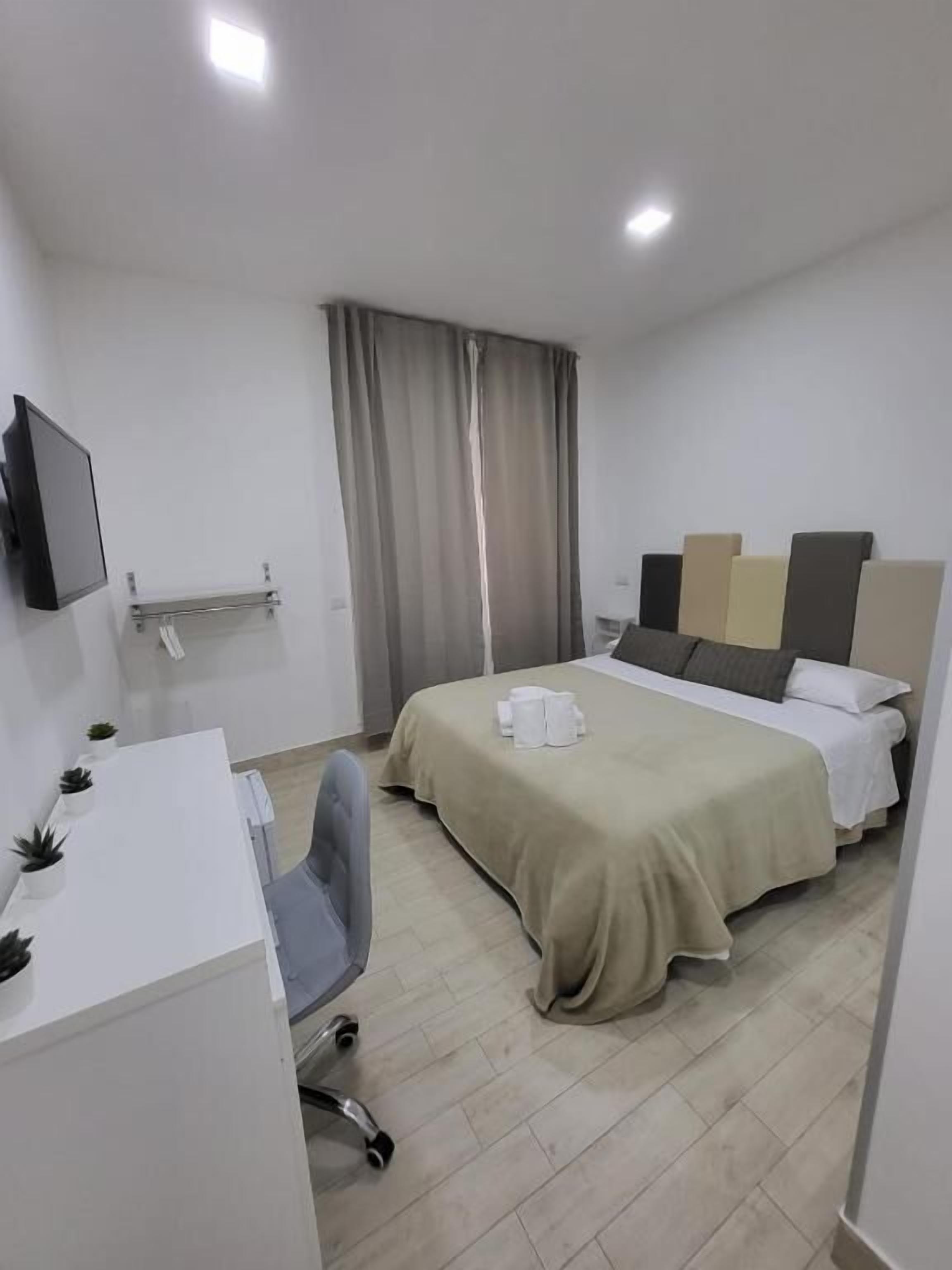 A hotel room with a bed, a desk with a chair, a TV, and a window with curtains.