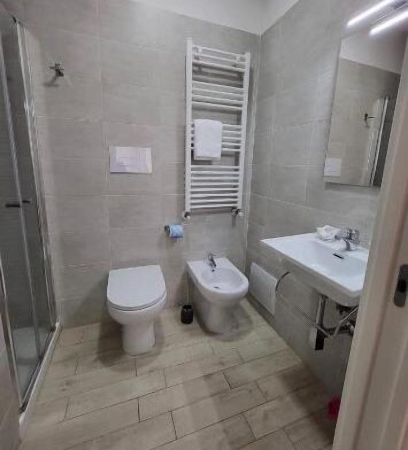 Un baño con inodoro, bidé y lavamanos, paredes de azulejos y una cabina de ducha de vidrio.