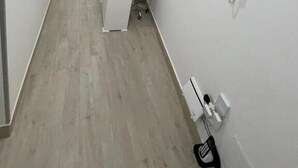 A hallway with a reception desk, a pink chair, and a wall-mounted phone. - New era Rooms  (Naples)