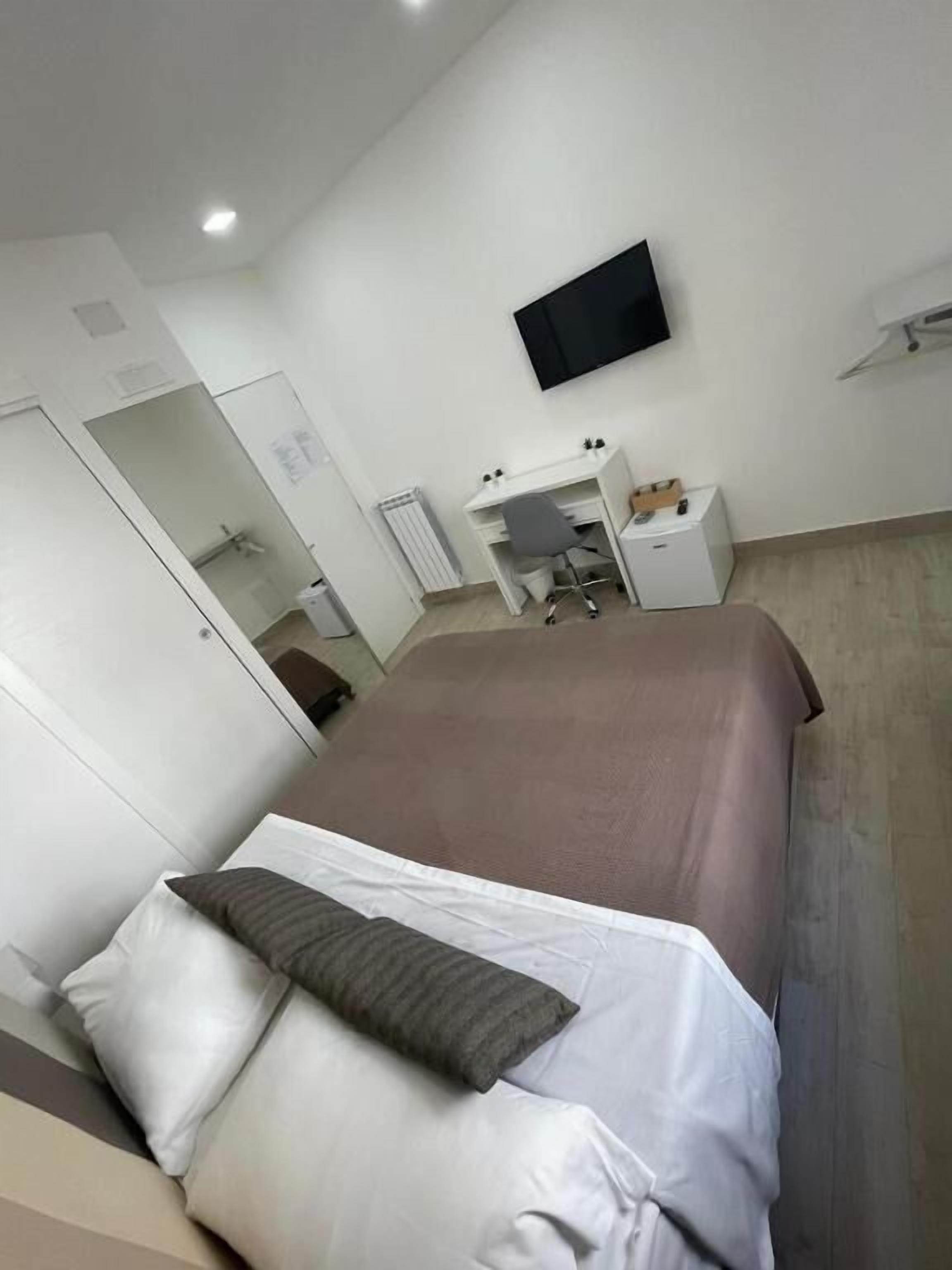 A modern hotel room with a large bed, a desk, and a television on the wall.