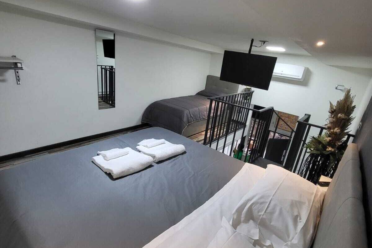 A modern hotel room with a large bed, a small desk, a flat-screen TV, and a balcony with a railing.