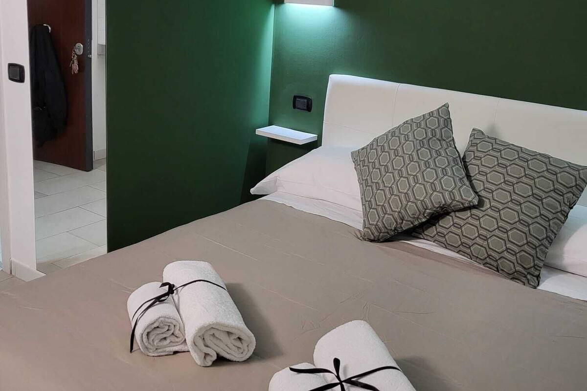 A hotel room with a green wall, a bed with two pillows, a nightstand, and two towels on the bed.