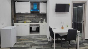 A compact kitchen with white cabinets, a gas stove, and a built-in oven. There's a dining table with two chairs and a flat-screen TV mounted on the wall. - New era Rooms  (Naples)