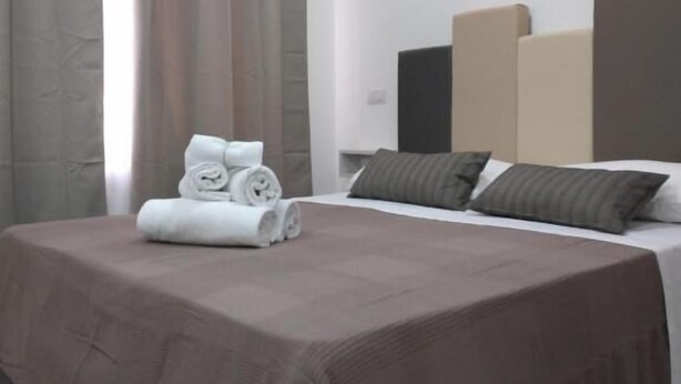 A hotel room with a neatly made bed, a headboard, and a window with curtains. - New era Rooms  (Naples)