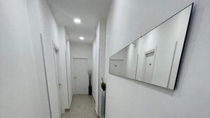 A narrow, well-lit hallway with white walls and a wooden floor. - New era Rooms  (Naples)