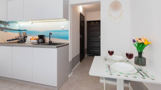 Una cocina moderna con un mural con motivos playeros, una zona de comedor con una mesa dispuesta para dos personas y un atrapasueños en la pared.