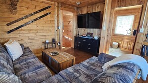 A cozy cabin interior with a wooden interior, a sofa, a coffee table, and a kitchen area with a TV. - Overlook Cabin - Lake/Mountain View*Pet Friendly*A/C*Washer/Dryer (Greenville)