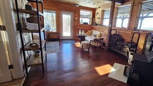 A cozy cabin interior with a wooden floor, a sofa, a chair, a fan, and a fireplace. - Overlook Cabin - Lake/Mountain View*Pet Friendly*A/C*Washer/Dryer (Greenville)