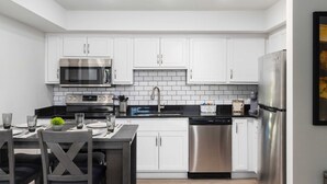Uma cozinha moderna com armários brancos, eletrodomésticos de aço inoxidável e bancada preta.