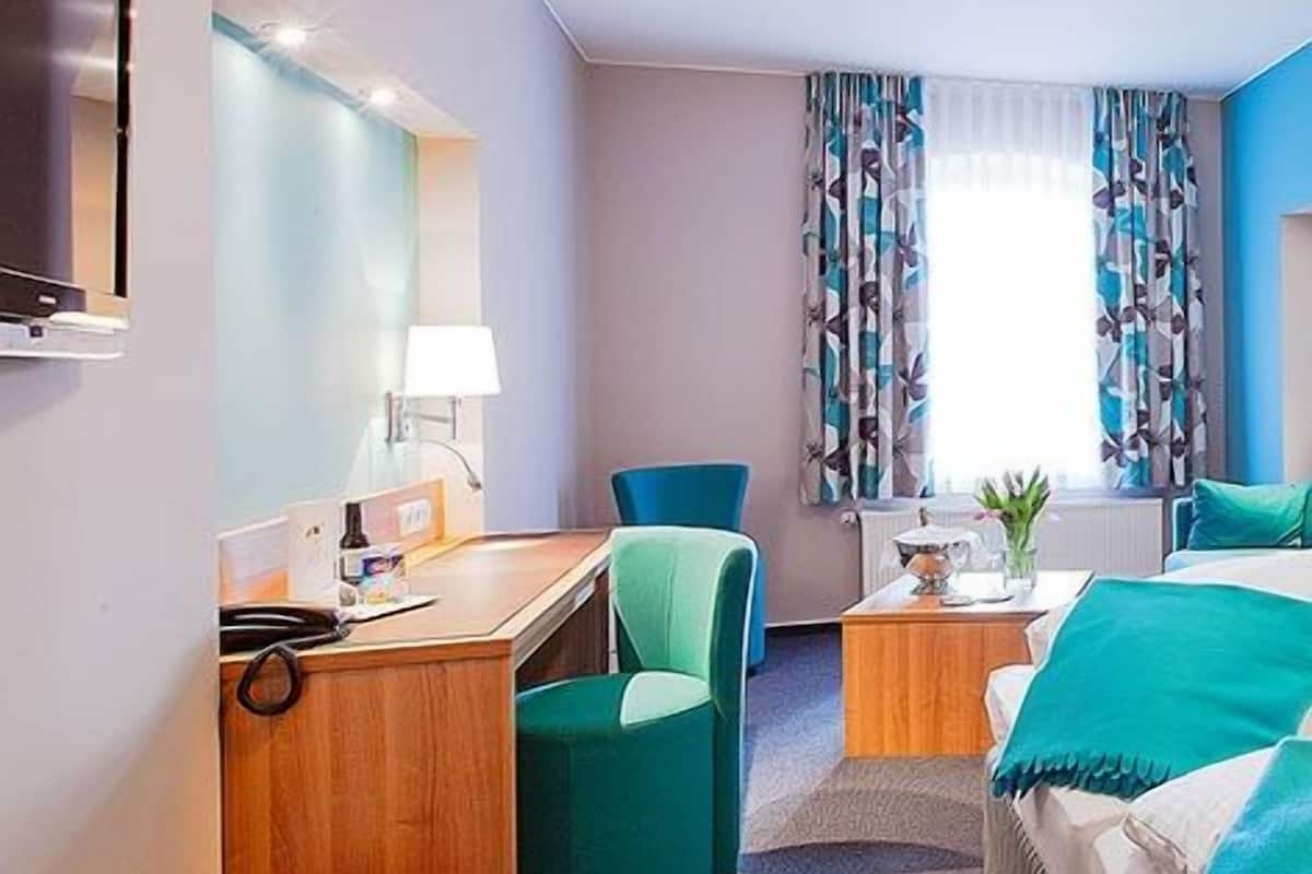 Ein Hotelzimmer mit Schreibtisch, Stuhl, Bett und einem kleinen Tisch mit Lampe.