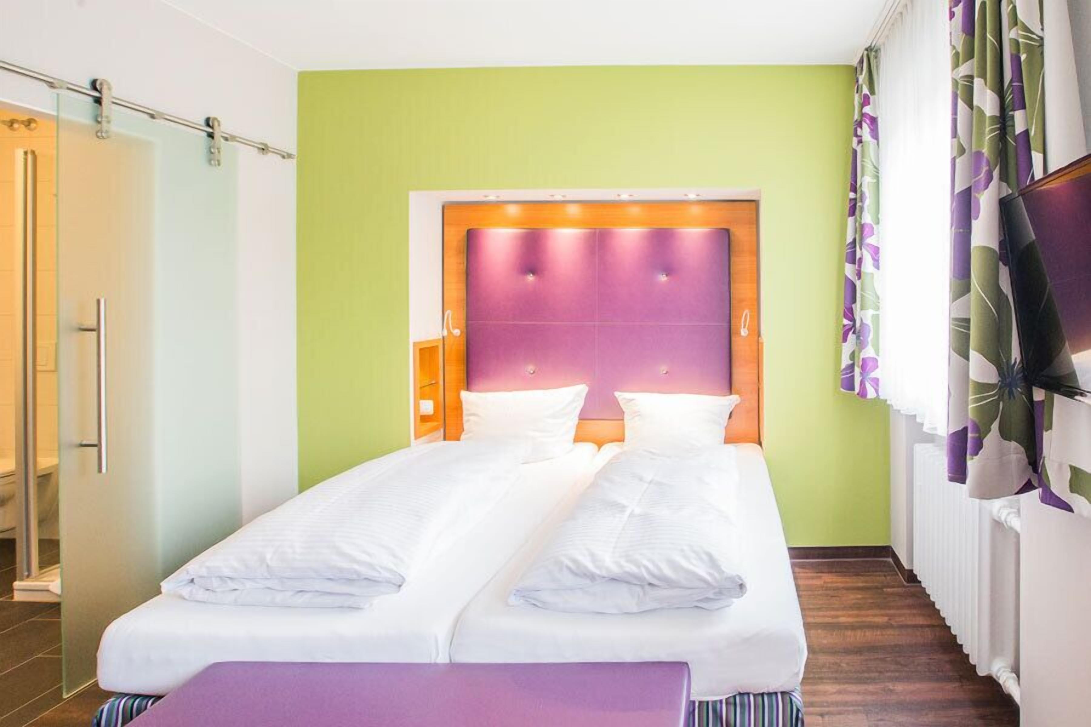Quarto de hotel com cama de casal, mesa de cabeceira, televisão e área de chuveiro.