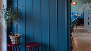 Een kamer met een blauwe wandpaneel, een rode vloerlamp, een potplant en een rieten mandje op een klein tafeltje.
