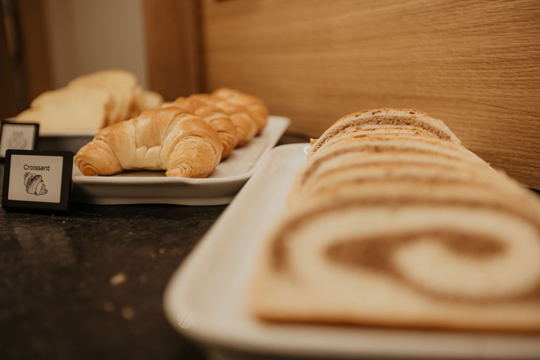 Diversos produtos de pastelaria, incluindo croissants e um pastel enrolado, numa bandeja.