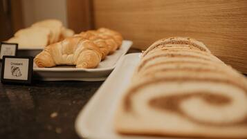 Diversos produtos de pastelaria, incluindo croissants e um pastel enrolado, numa bandeja.