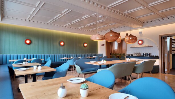 Een modern restaurant met blauwe zitplaatsen, houten tafels en decoratieve verlichting.