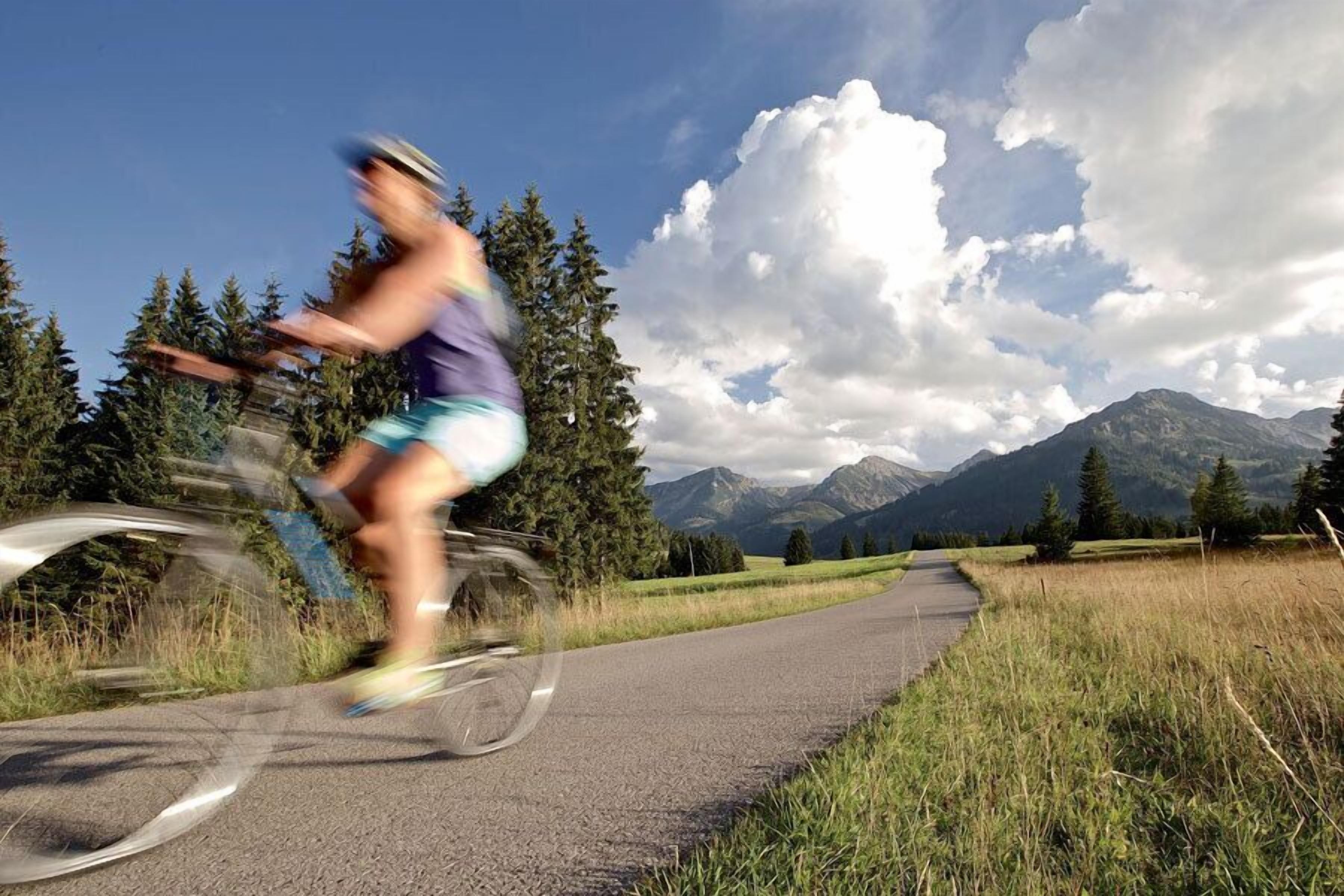 A cyclist on a paved path with a mountainous landscape in the background.