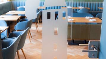 A modern restaurant interior with wooden flooring, blue upholstered booths, and a decorative castle cutout on the wall.