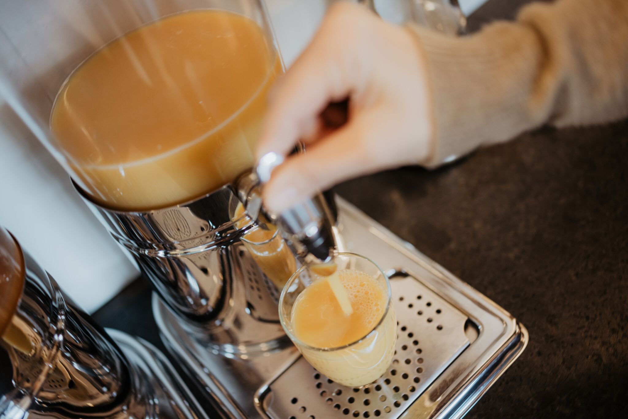 A hand pouring a beverage from a metallic dispenser into a glass.