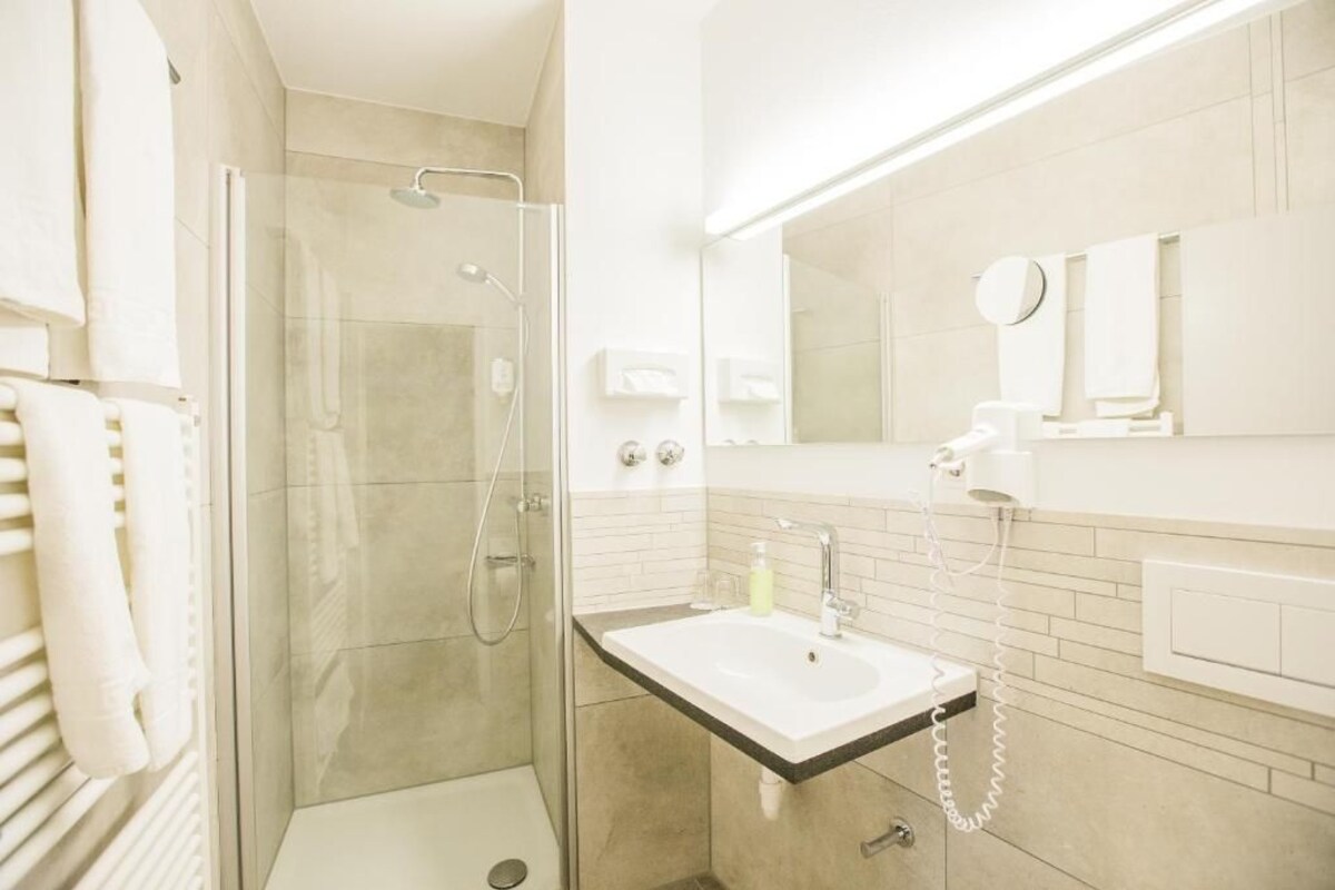 A modern bathroom with a glass-enclosed shower, a white sink with a mirror above it, and a towel rack.