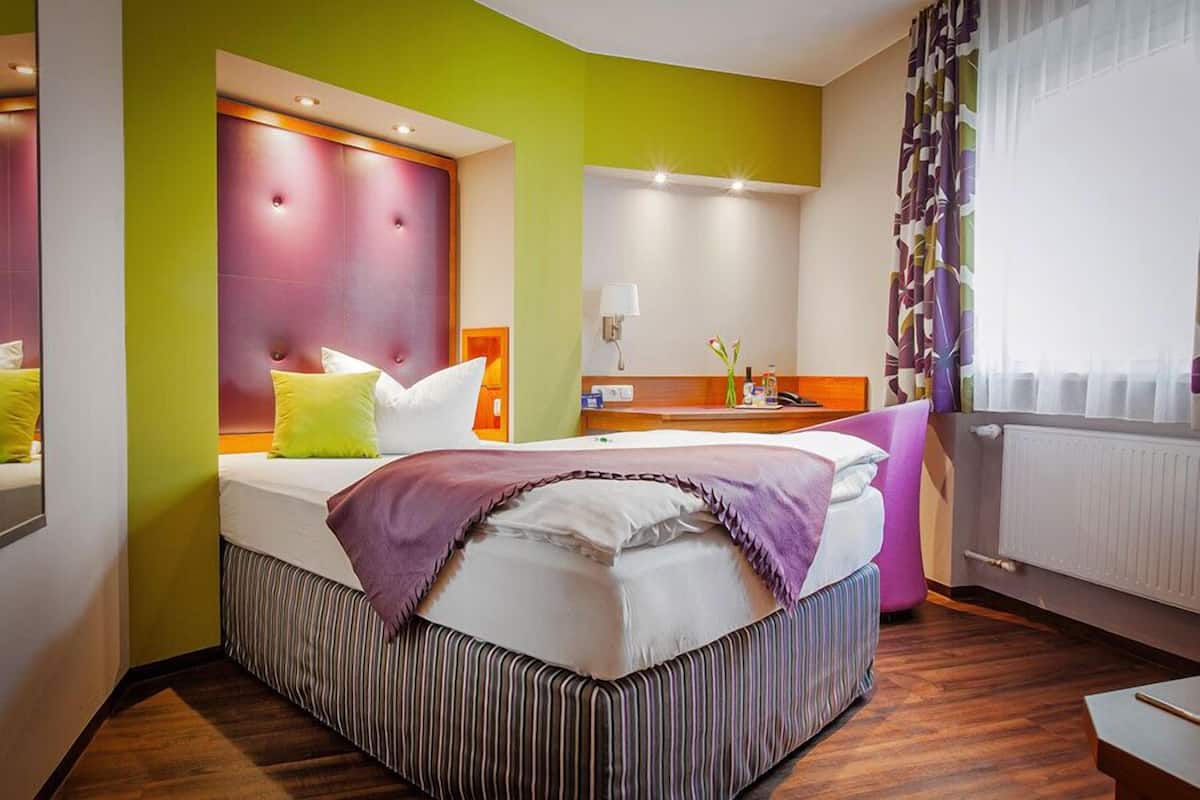 Ein Hotelzimmer mit Bett, Nachttisch, Spiegel und einem Fenster mit Vorhängen.