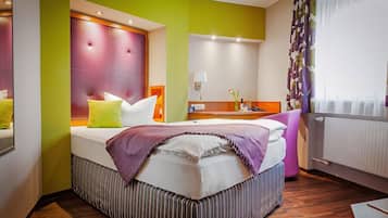A hotel room with a bed, a bedside table, a mirror, and a window with curtains.