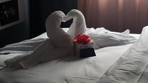 A bed with a white blanket, a heart-shaped towel arrangement, a small gift box, and a red bow. - BLOOM Boutique Hotel & Lounge Basel (Basel)