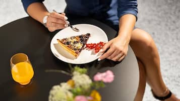 A person sitting at a round table with a slice of pizza, a glass of orange juice, and a small vase of flowers.