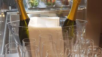 Dos botellas de champán en un portavasos con varios vasos de vino vacíos frente a una mesa de buffet.