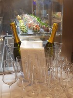 Dos botellas de champán en un portavasos con varios vasos de vino vacíos frente a una mesa de buffet.