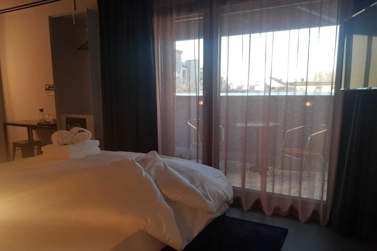 A hotel room with a large bed, a desk, and a view of the city through the window.