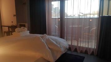 A hotel room with a large bed, a desk, and a view of the city through the window.