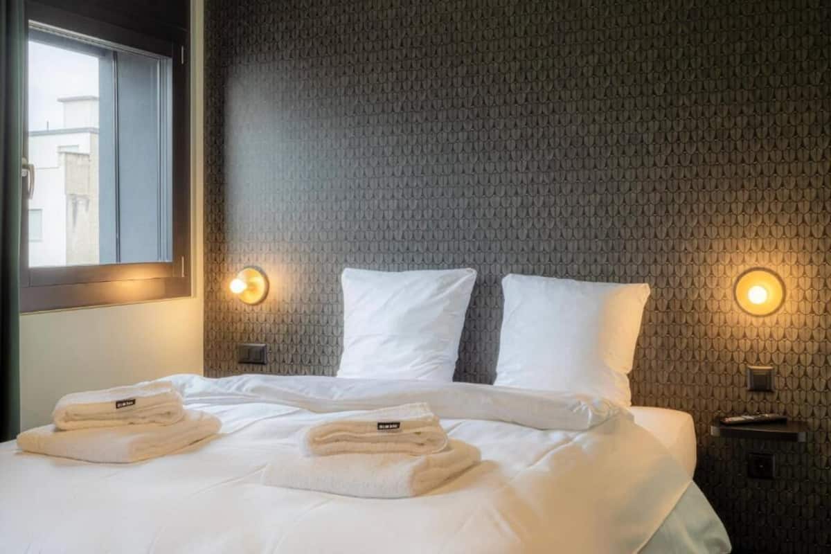 A hotel room with a bed, two pillows, two bedside tables, and a window.