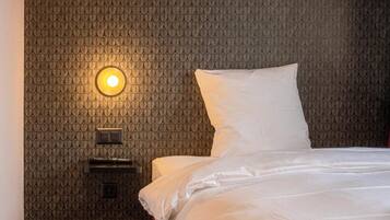 Habitación de hotel con pared estampada, cama con ropa blanca y lámpara de pared.