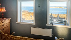 A room with two windows overlooking a beach, a wooden dresser, a radiator, and a lamp. - Nice home in Smøla with house sea view (Smøla)