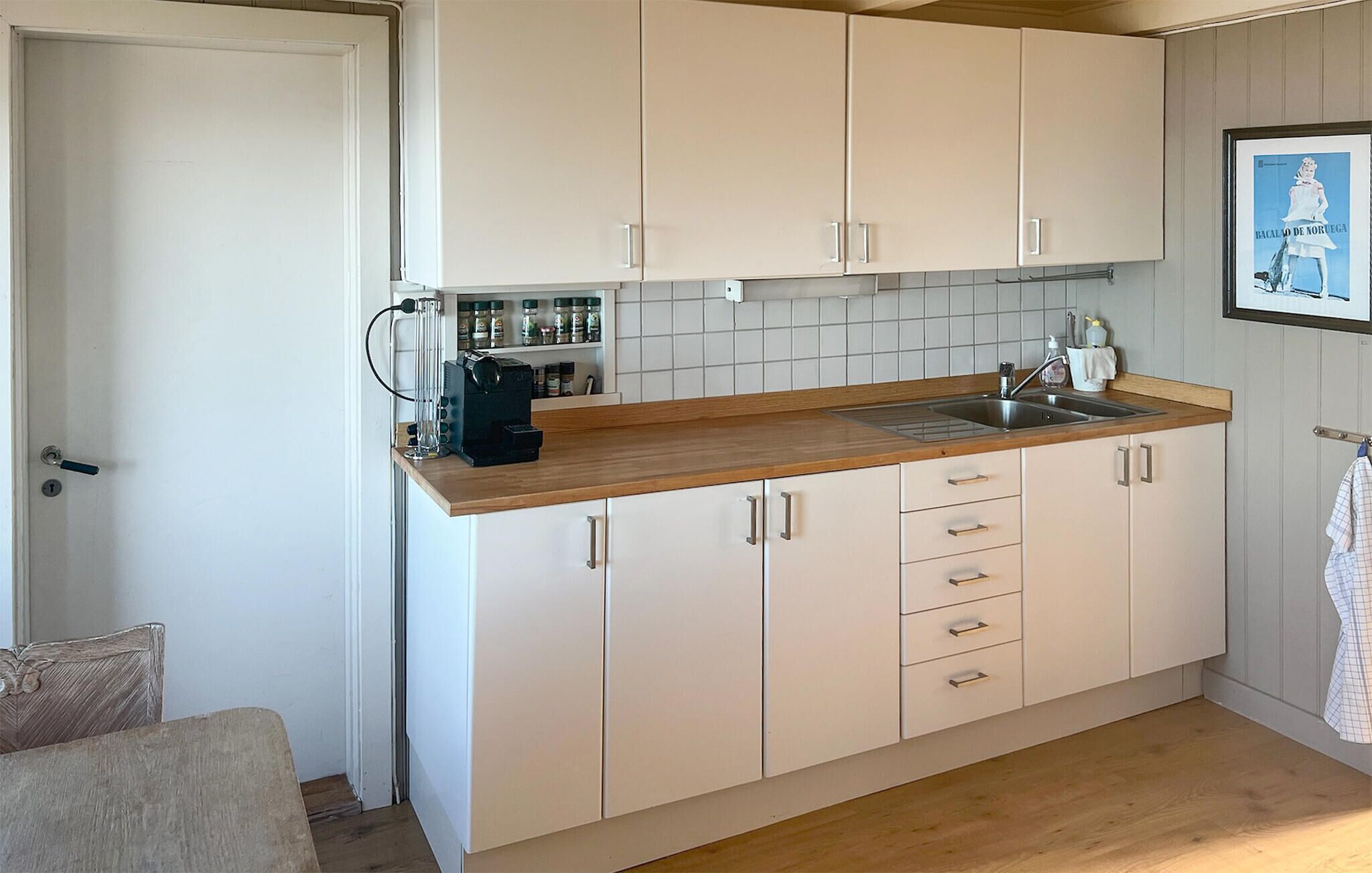 Une cuisine compacte avec des meubles blancs, un plan de travail en bois et une machine à café.