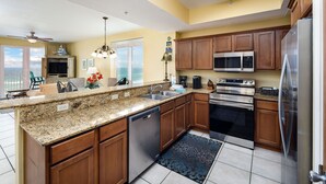 A kitchen with granite countertops, wooden cabinets, stainless steel appliances, and a view to the outside. - SDN 504: Vacation Vibe - Spectacular Corner Unit with MARVELOUS Beach Views! (Fort Walton Beach)