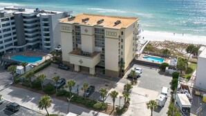 A hotel with a rooftop pool, a beach view, and a parking lot with several cars. - SDN 504: Vacation Vibe - Spectacular Corner Unit with MARVELOUS Beach Views! (Fort Walton Beach)